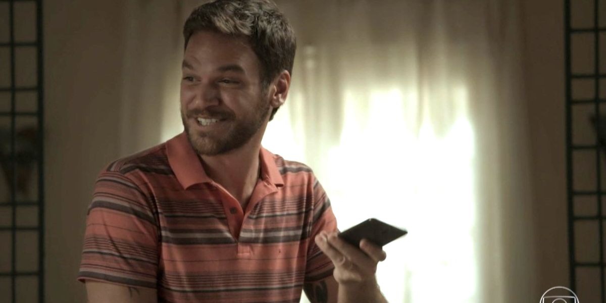 Rubinho em cena de A Força do Querer com telefone na mão e sorrindo