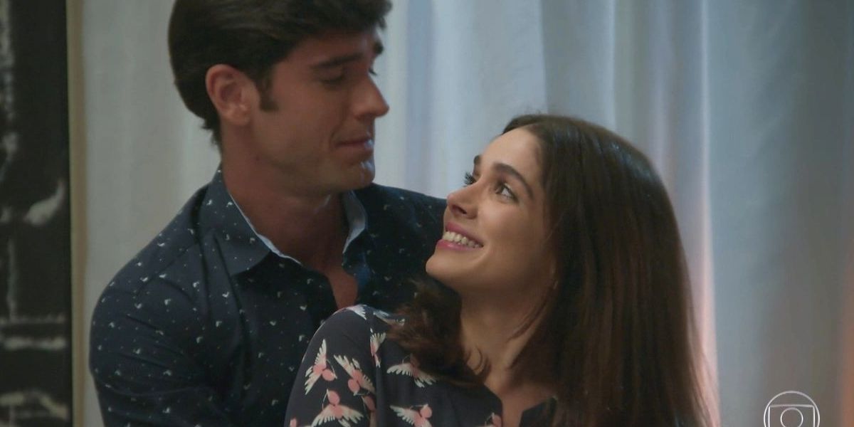 Felipe e Shirlei de Haja Coração estão abraçados em cena da novela e se encarando, ela sorri para ele