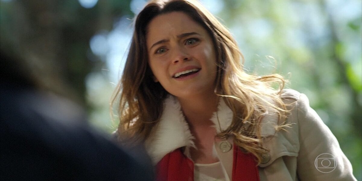 Ana com blusa creme de frio ao ar livre em cena de A Vida da Gente
