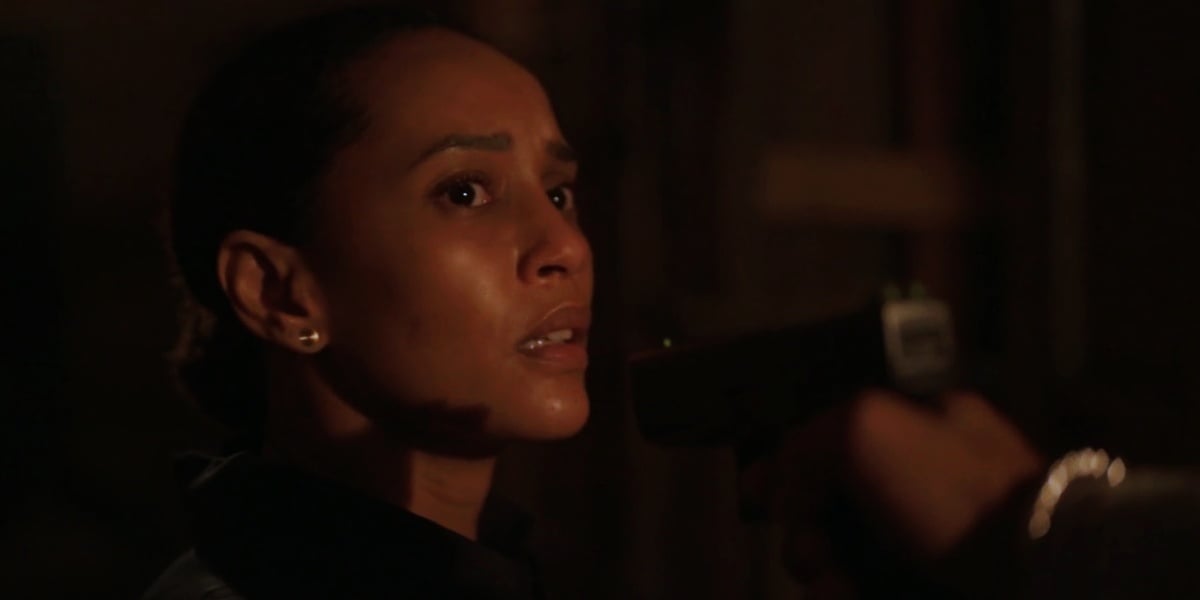 Vitória de Amor de Mãe, está em cena escura da novela com arma apontada para o seu rosto, ela é uma mulher negra que tem expressão de apreensão