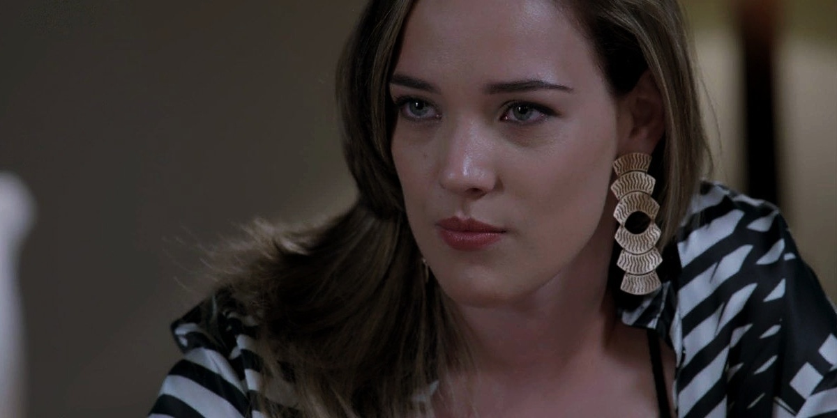 Amanda, mulher loira com brincos grandes e camisa preta e branca listrada, em cena de Império 