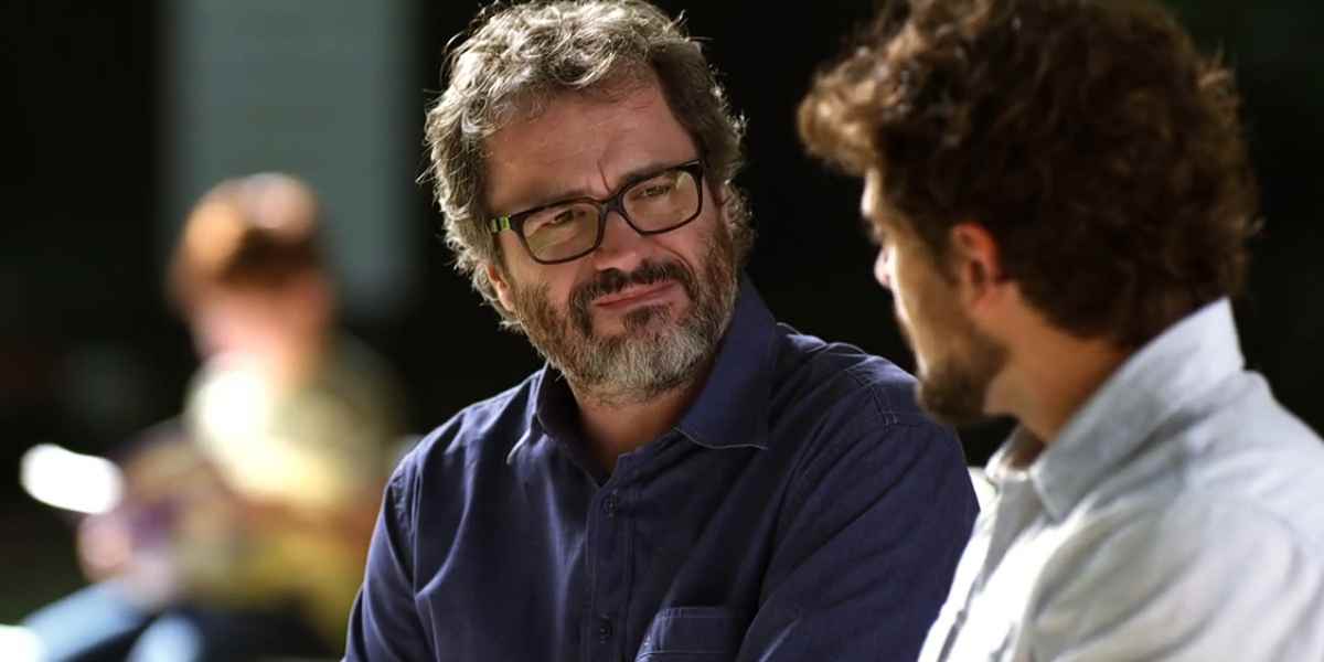 Lourenço usa camisa azul e óculos pretos está em cena da novela A Vida da Gente ao ar livre
