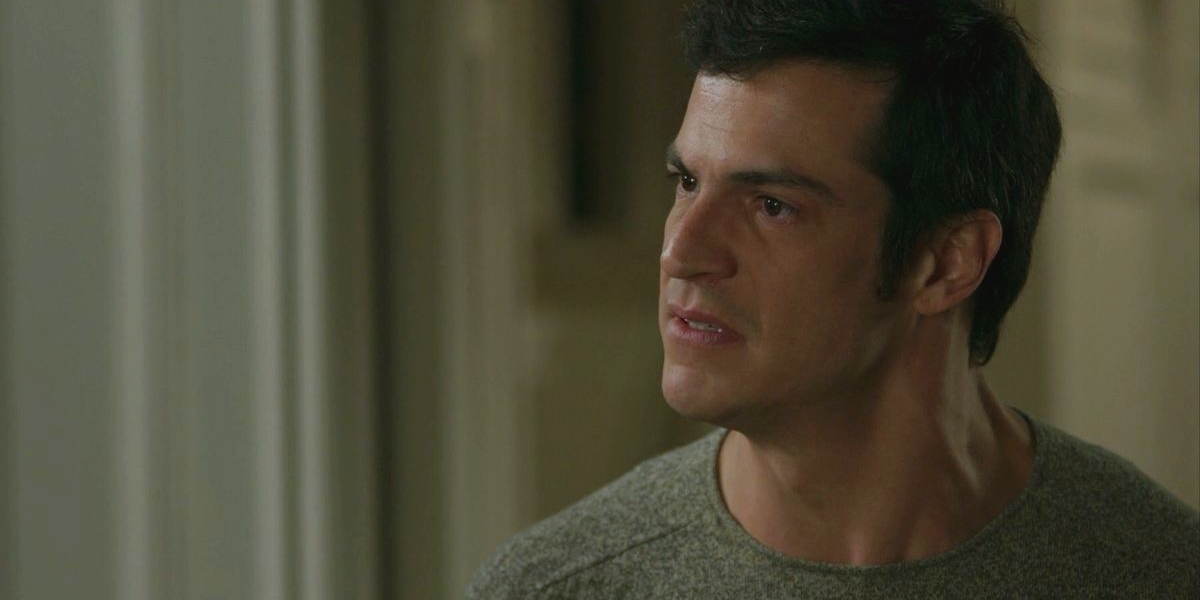 Eric usa camisa cinza e cabelo liso preto em cena de Pega Pega