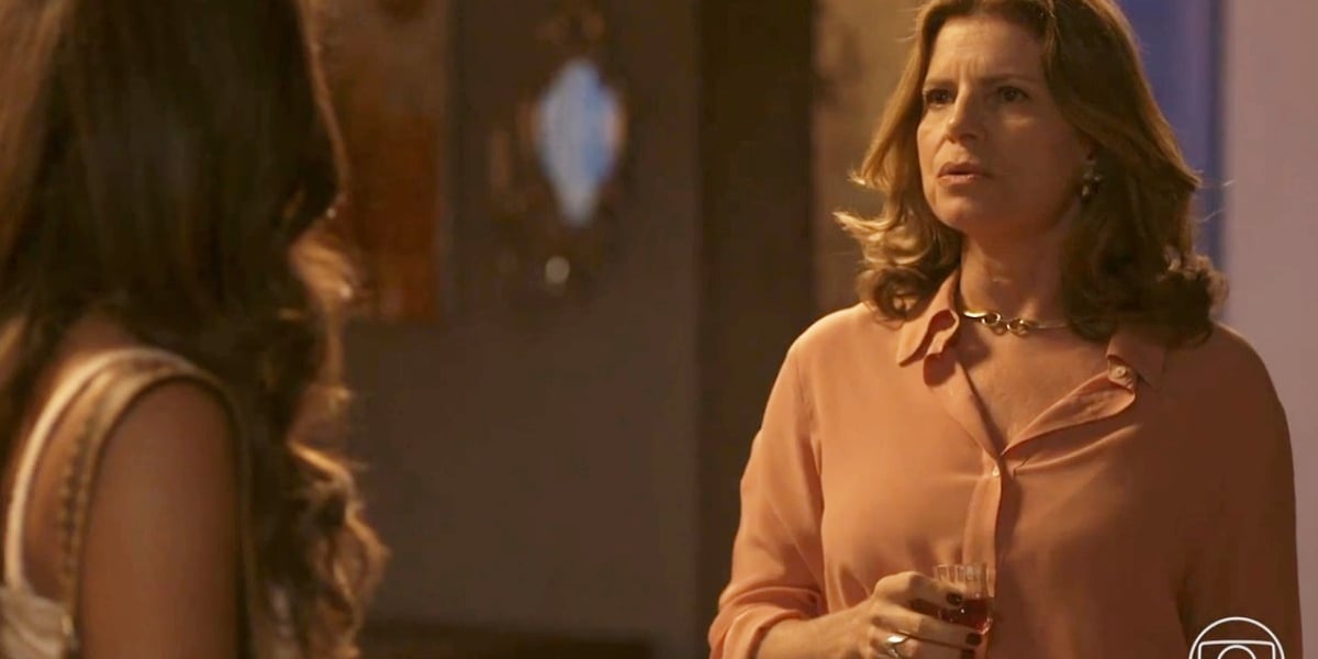 Deodora usando camisa rosa e segurando uma pequena taça encara Candoca em Mar do Sertão