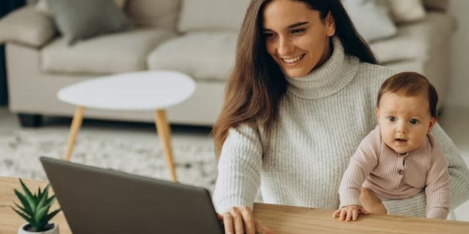 Mulher usando computador com bebê no colo (Foto: Reprodução / Freepik)