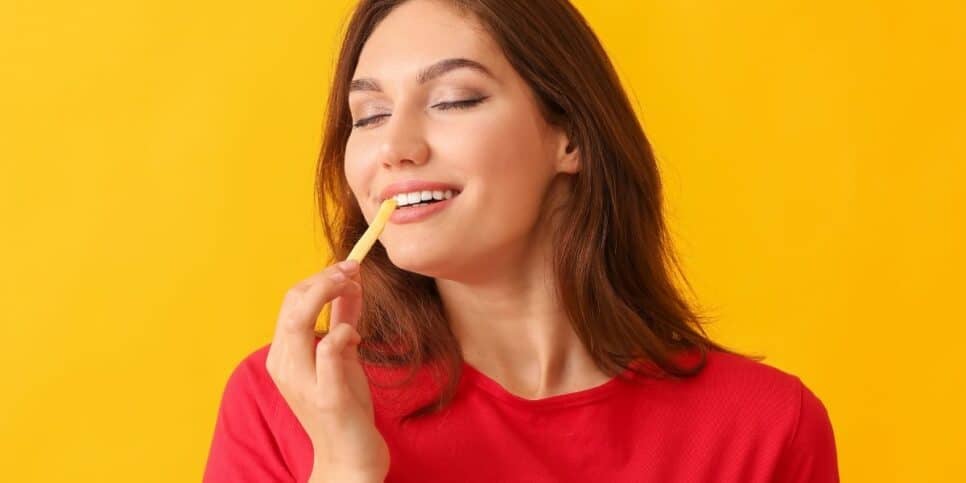 Mulher comendo batata frita (Foto: Canva) 