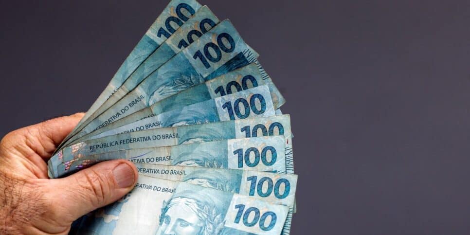 Pessoa segurando notas de cem reais (Foto: Canva)