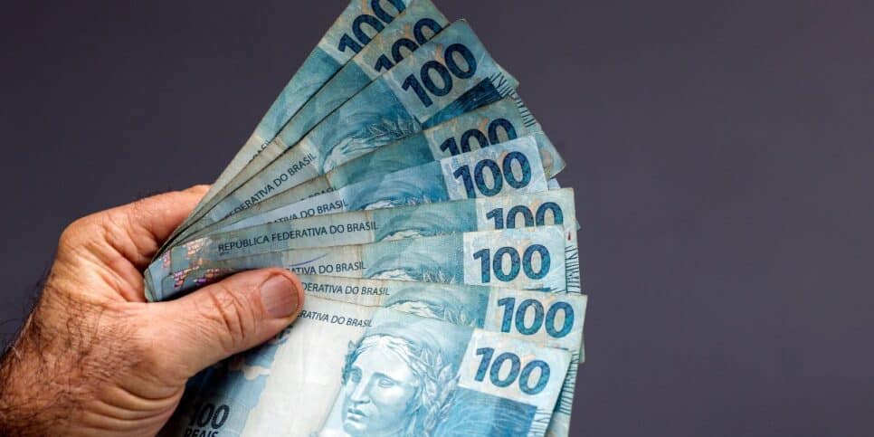 Homem segurando notas de cem reais (Foto: Canva)