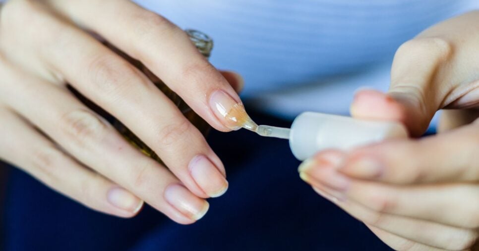 Mulher passando base nas unhas (Foto: Canva)