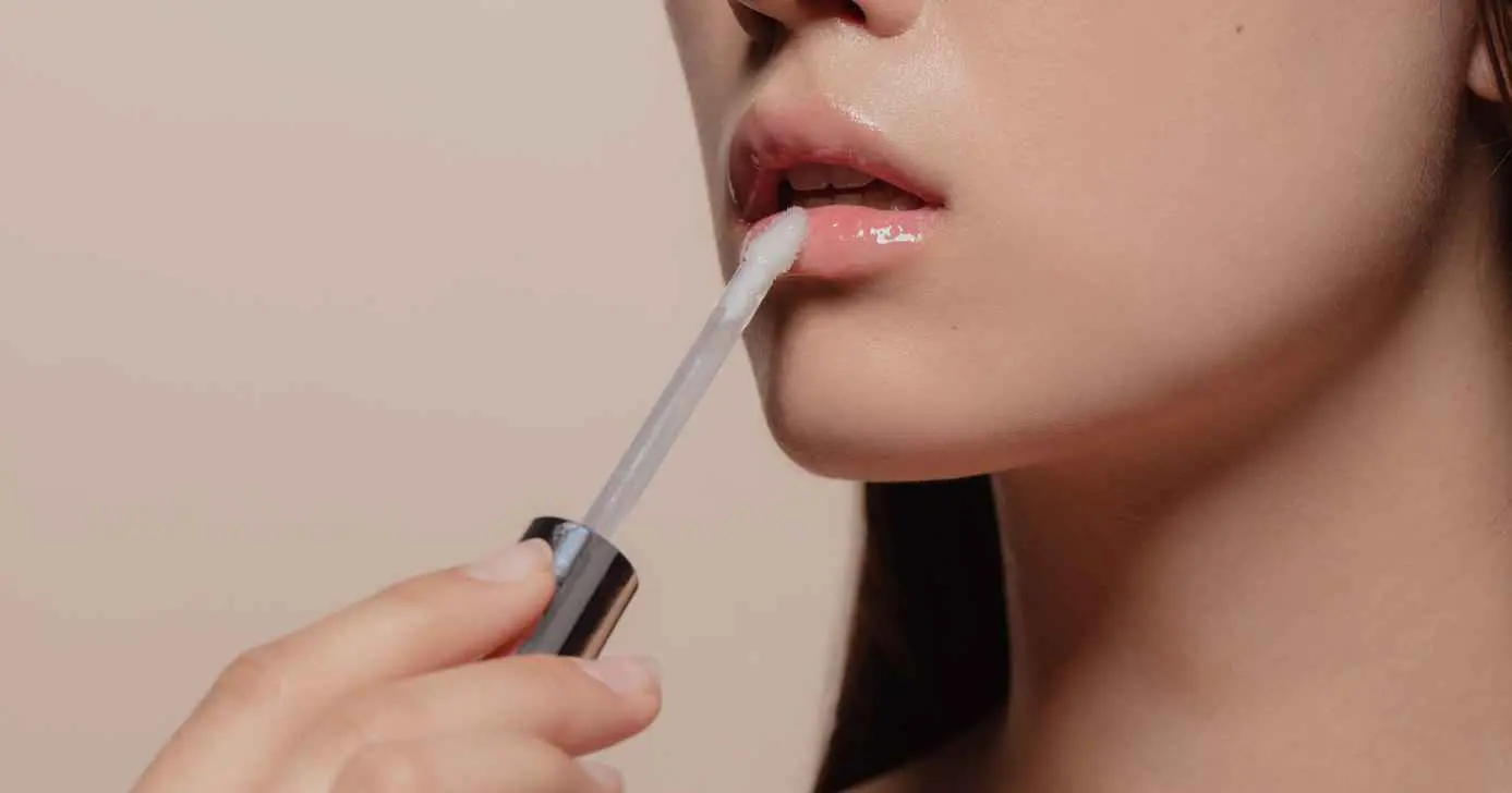 Mulher passando gloss nos lábios (Foto: Canva)